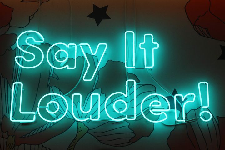 A neon sign that reads, "say it louder."